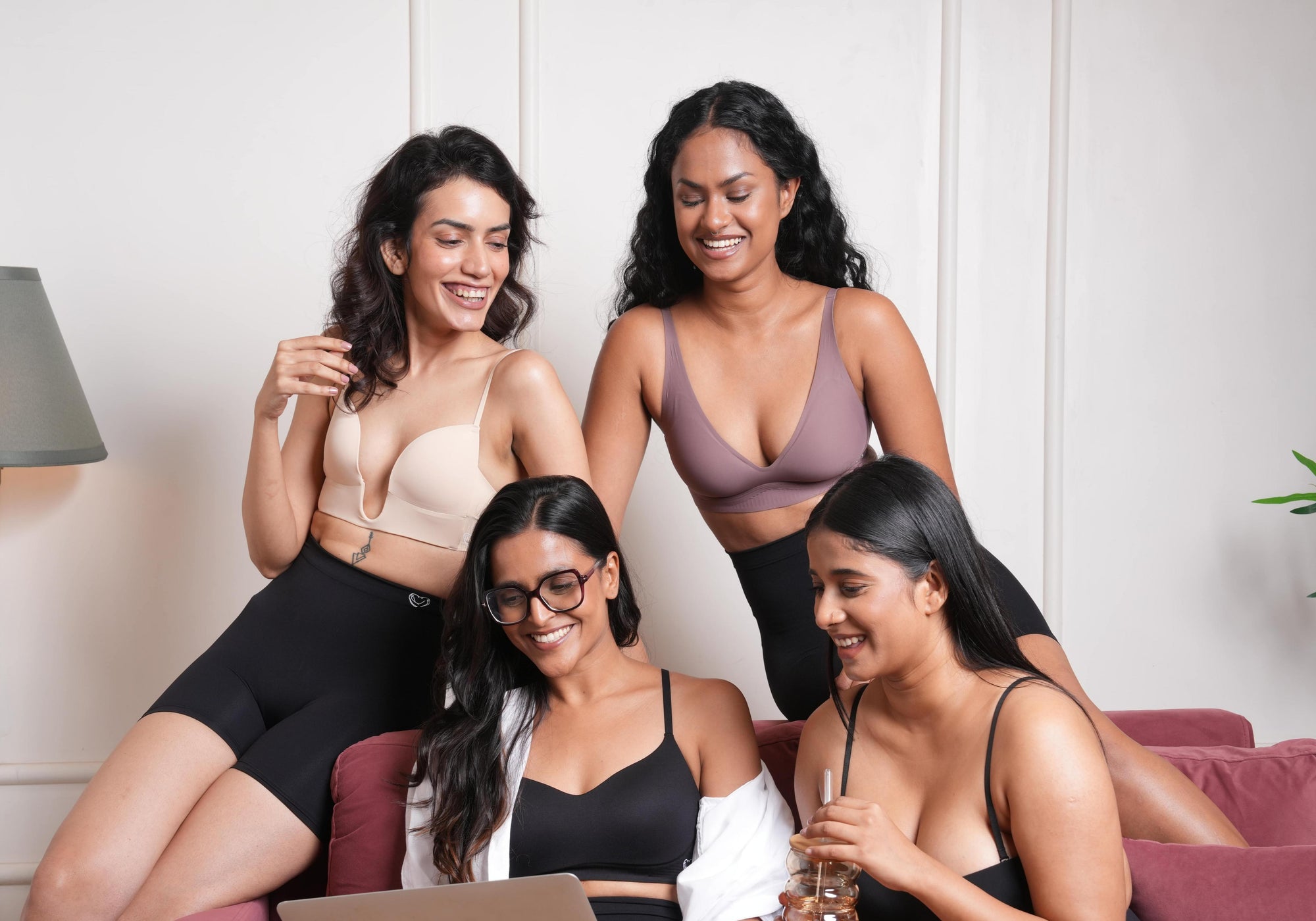 Four women sitting on a couch with a laptop, smiling and interacting.